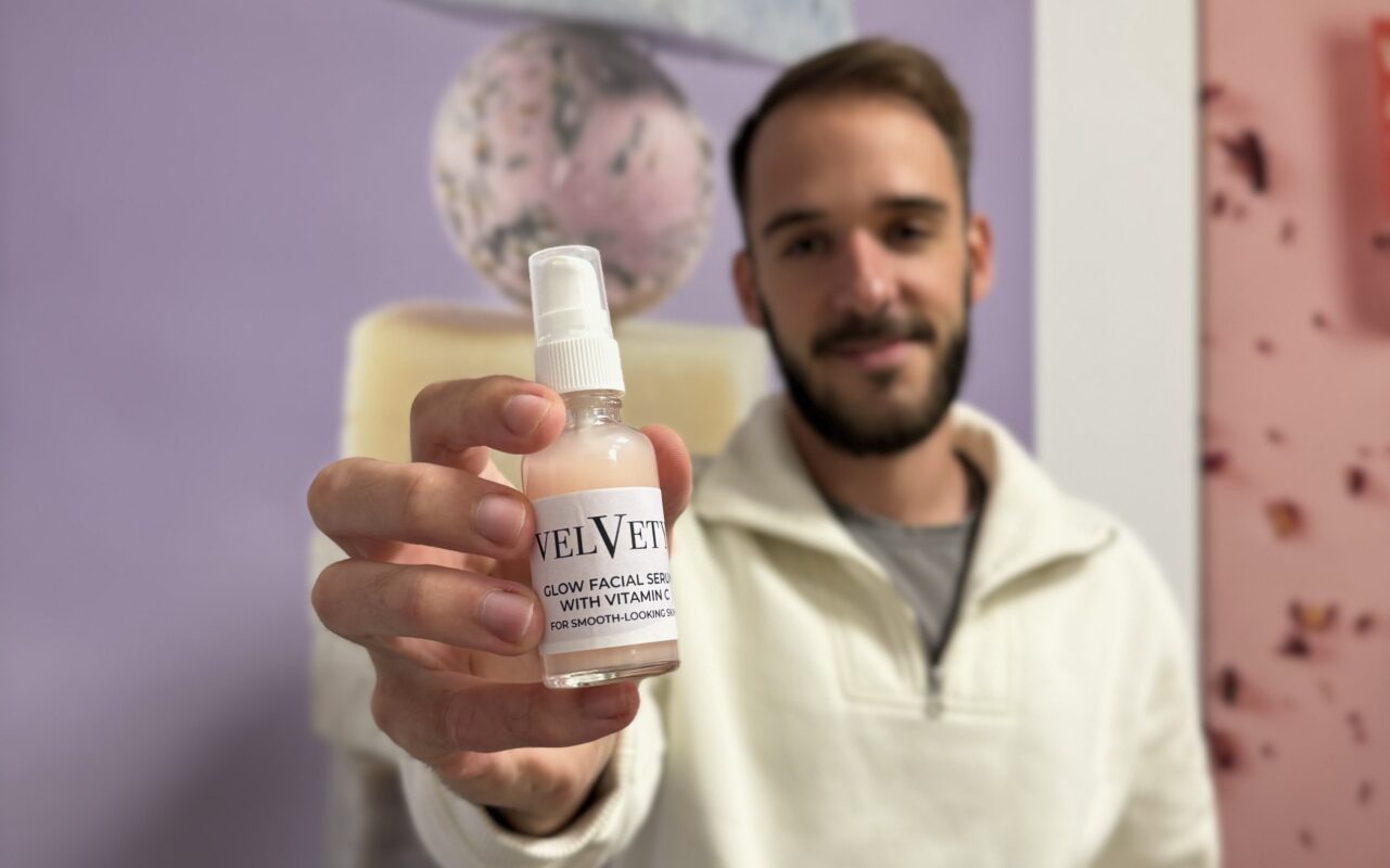 Mitarbeiter hält ein Velvety Glow Facial Serum mit Vitamin C in die Kamera, unscharfer Hintergrund, Fokus auf dem Produkt