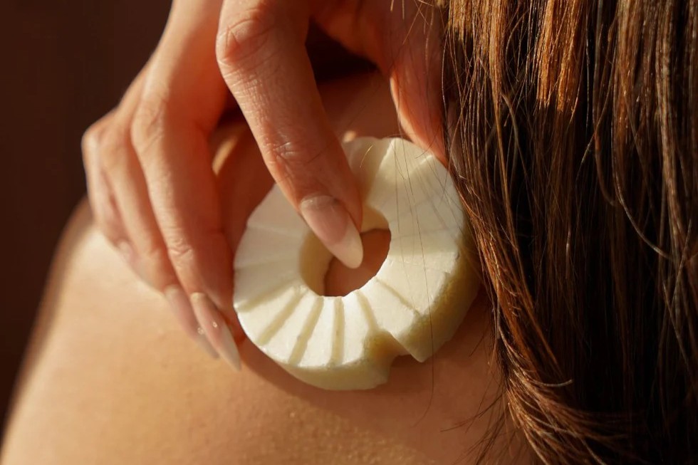 Nahaufnahme einer festen Shampoo Bar von Lesseau, die sanft über nasses Haar und die Kopfhaut geführt wird.