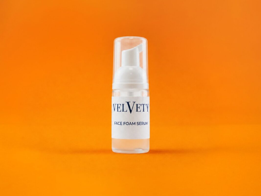 Velvety Face Foam Serum vor orangefarbenem Hintergrund.