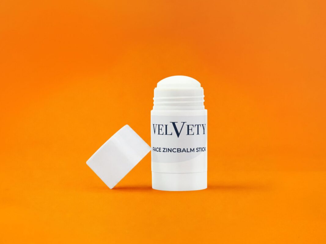 Velvety Face Zincbalm Stick vor orangefarbenem Hintergrund.