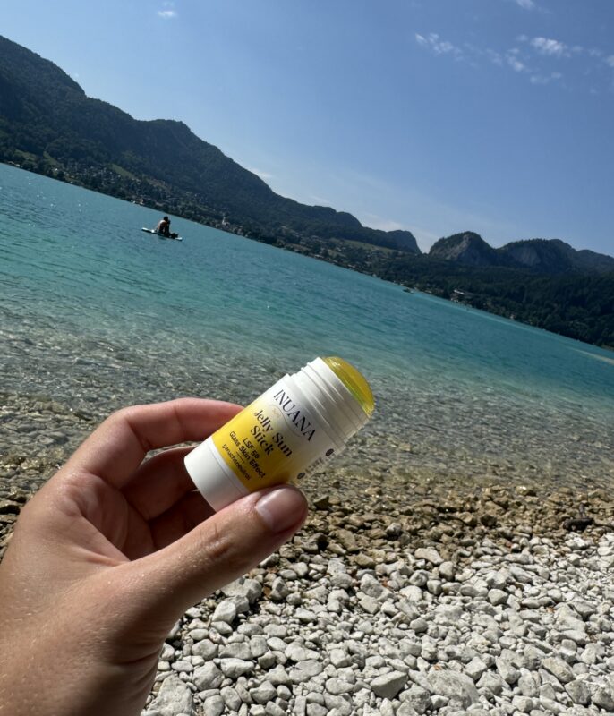 Hand hält den INUANA Jelly Sun Stick LSF 50 vor einem klaren Bergsee.