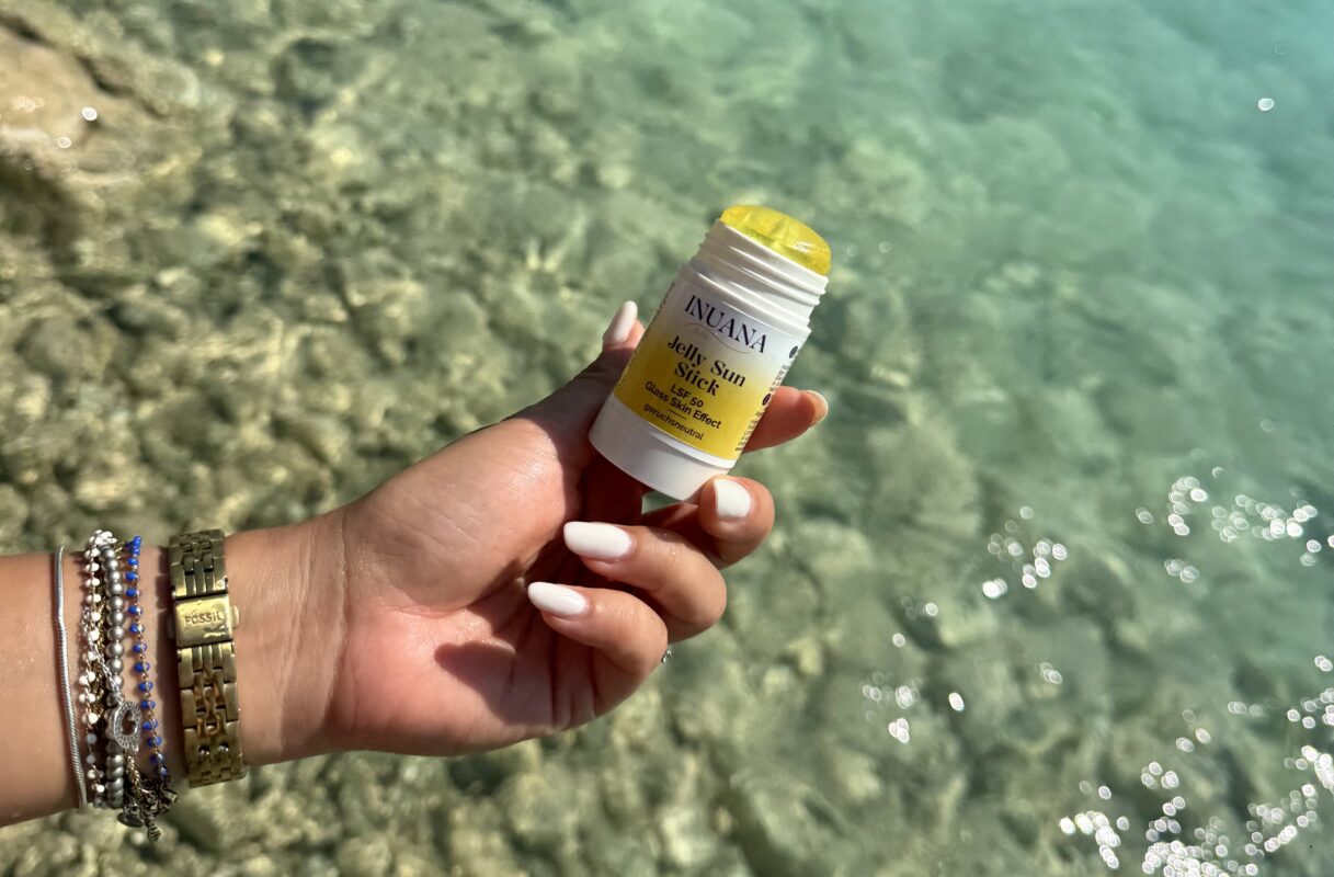 Hand hält den INUANA Jelly Sun Stick LSF 50 vor klarem Meerwasser.