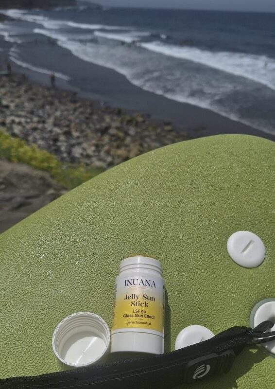 INUANA Jelly Sun Stick LSF 50 auf einem Surfbrett vor dem Meer.
