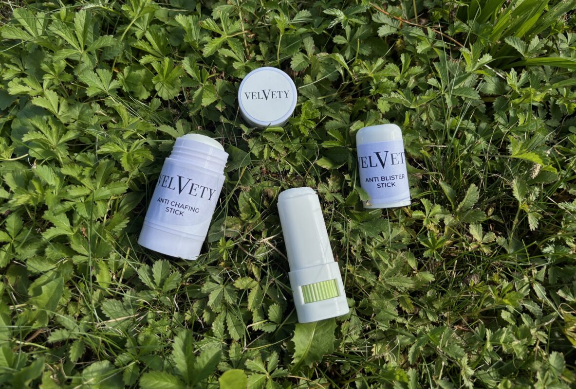 Anti-Wundreib-Stick und Anti-Blasen-Stick von Velvety in verschiedenen Verpackungen auf einer grünen Wiese.